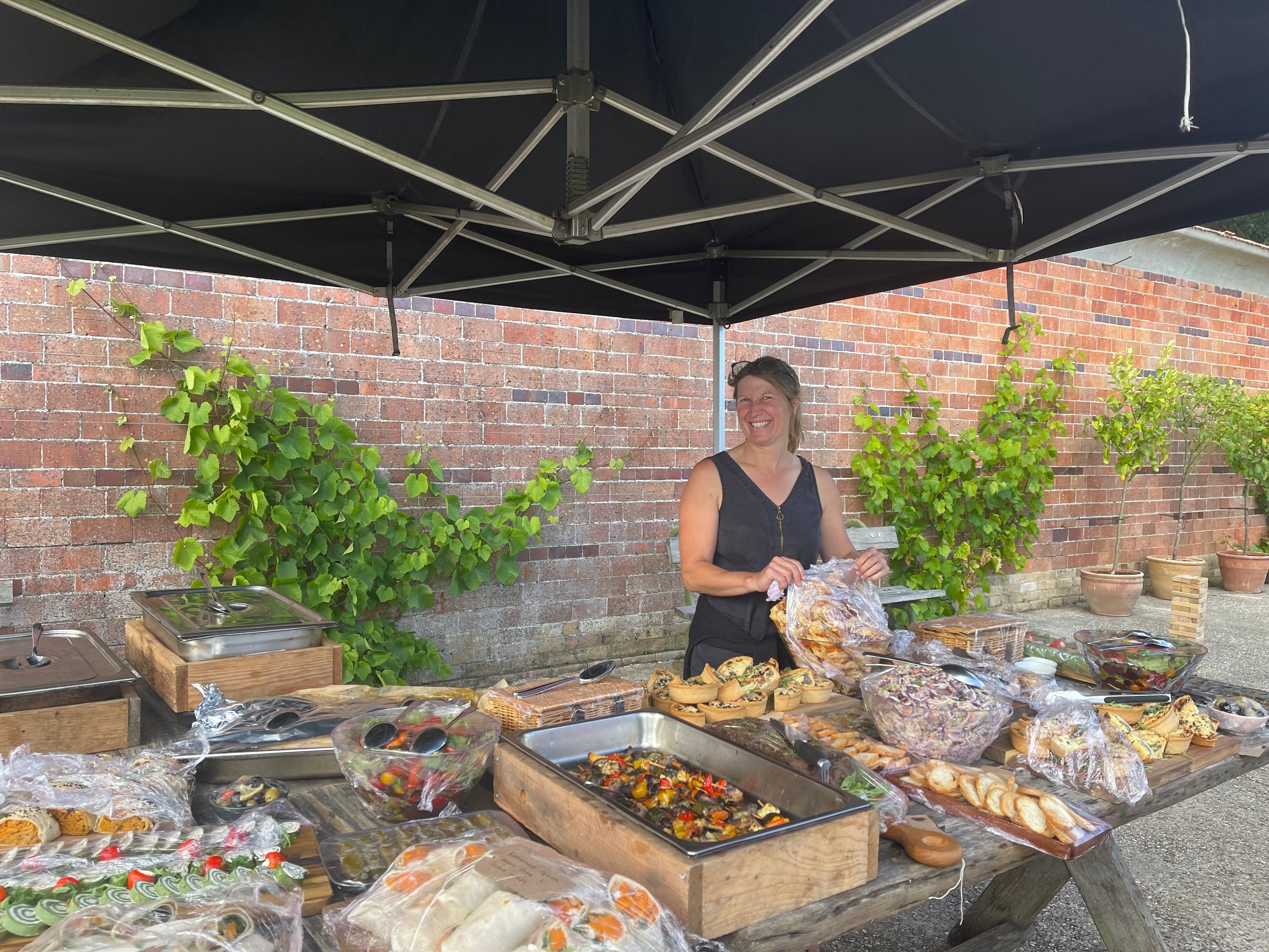 Woman hosting a buffet in Carey’s Secret Garden, setting up a vibrant spread outdoors amidst the lush garden setting, creating a welcoming and festive atmosphere for guests