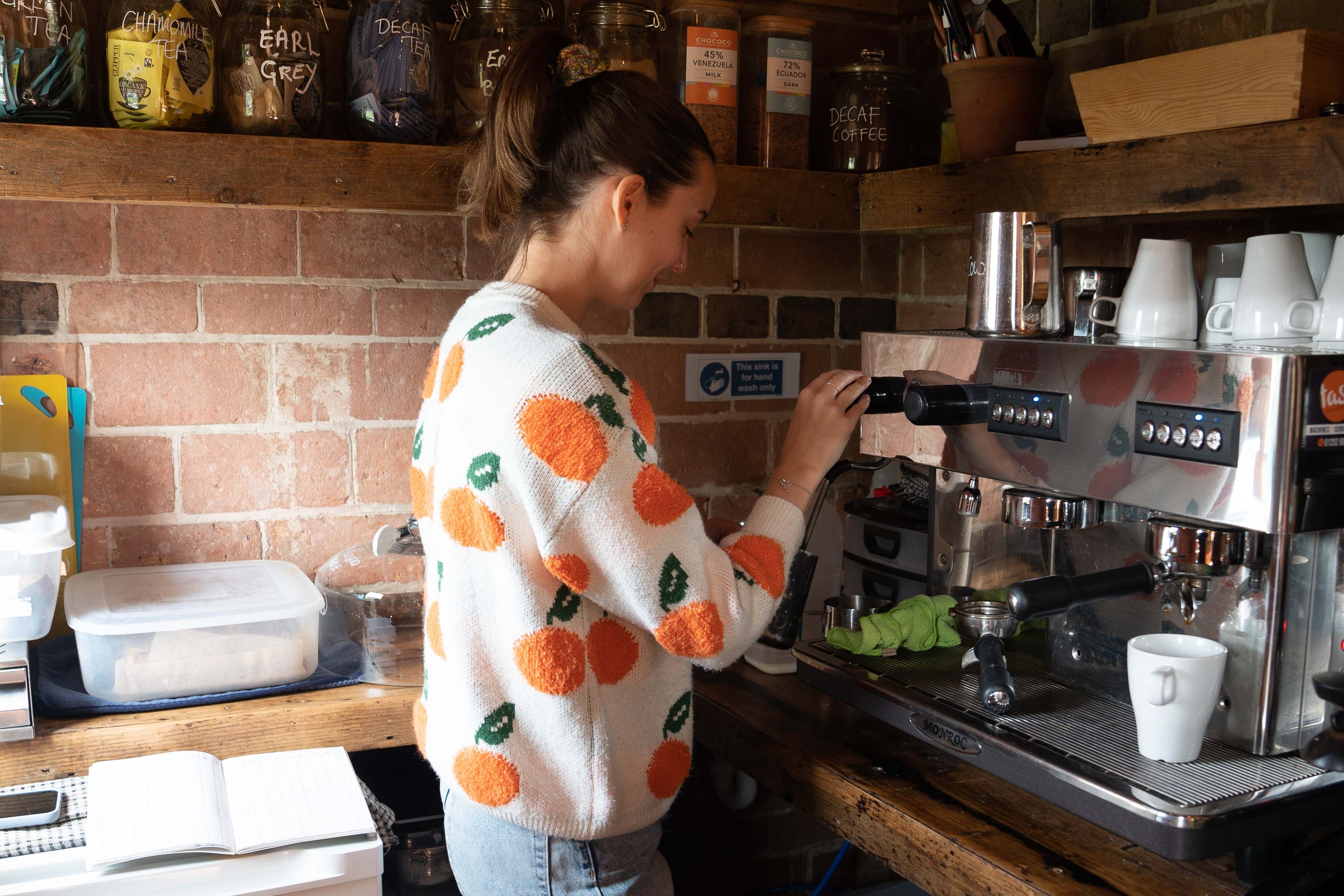 Young woman using the coffee machine in the coffee shop at Carey’s, preparing a fresh cup of barista coffee in a cosy, welcoming space surrounded by natural beauty.