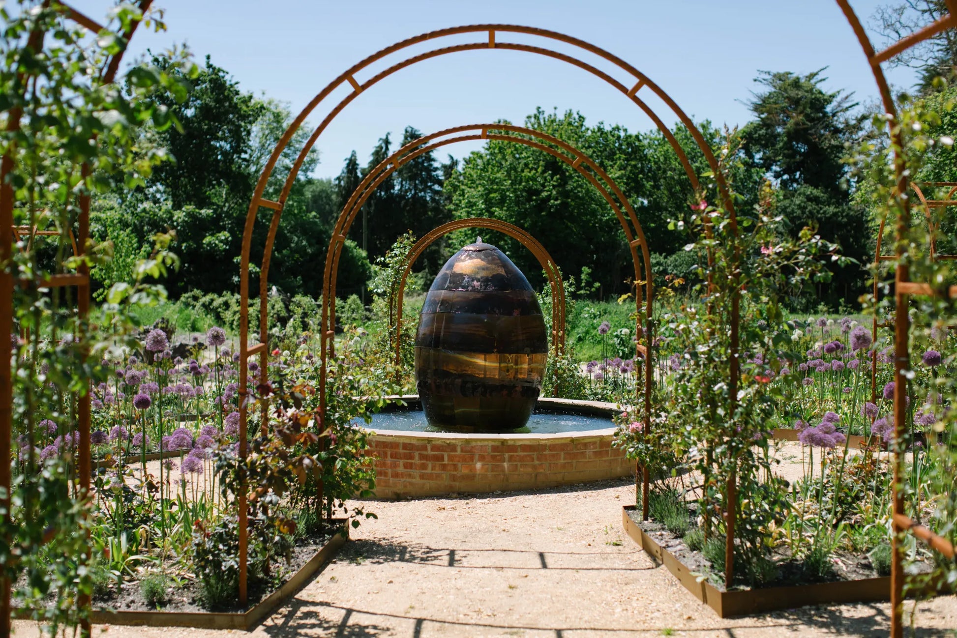 Rose wheel and water feature at the center of Carey’s Secret Garden, beautifully designed with vibrant flowers and flowing water, creating a peaceful, serene focal point in the garden