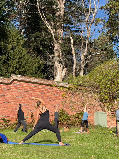 Women’s yoga class at Carey’s, with participants practicing poses outdoors in a serene garden setting, surrounded by nature and the peaceful ambiance of the garden.