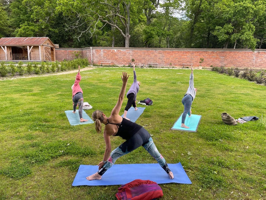 Women’s yoga class at Carey’s, with participants practicing poses outdoors in a serene garden setting, surrounded by nature and the peaceful ambiance of the garden.